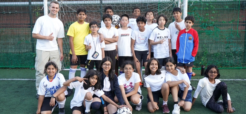A diverse group of kids and a coach pose for a team photo on a soccer field, showing smiles and enthusiasm.