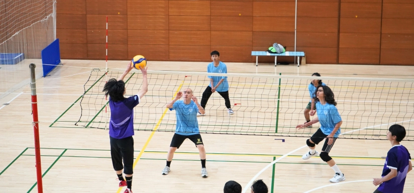 Players engaged in an intense volleyball match indoors, with one player jumping to spike the ball.