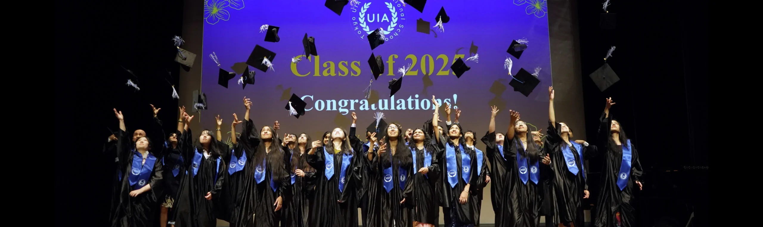 Graduates celebrate by tossing caps at the Class of 2025 ceremony. Congratulations banner in background.
