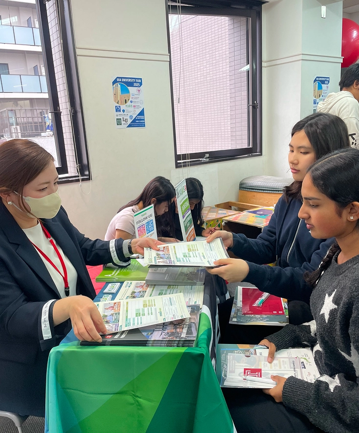 Students engage with a university representative at an educational fair, discussing academic programs and opportunities.