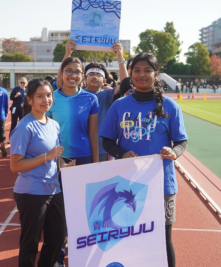 Group of students in blue at an outdoor event, holding a Seiryuu banner and sign on a track.