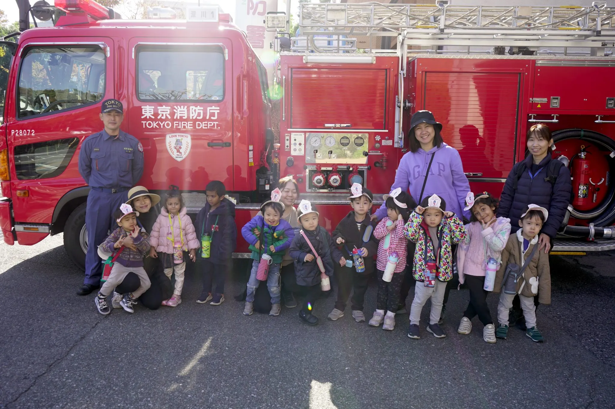 Kids and adults posing with a Tokyo Fire Department truck on a sunny day.