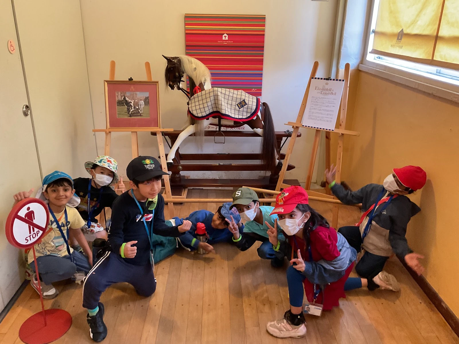 Children pose playfully by a rocking horse in a museum, wearing hats and masks.