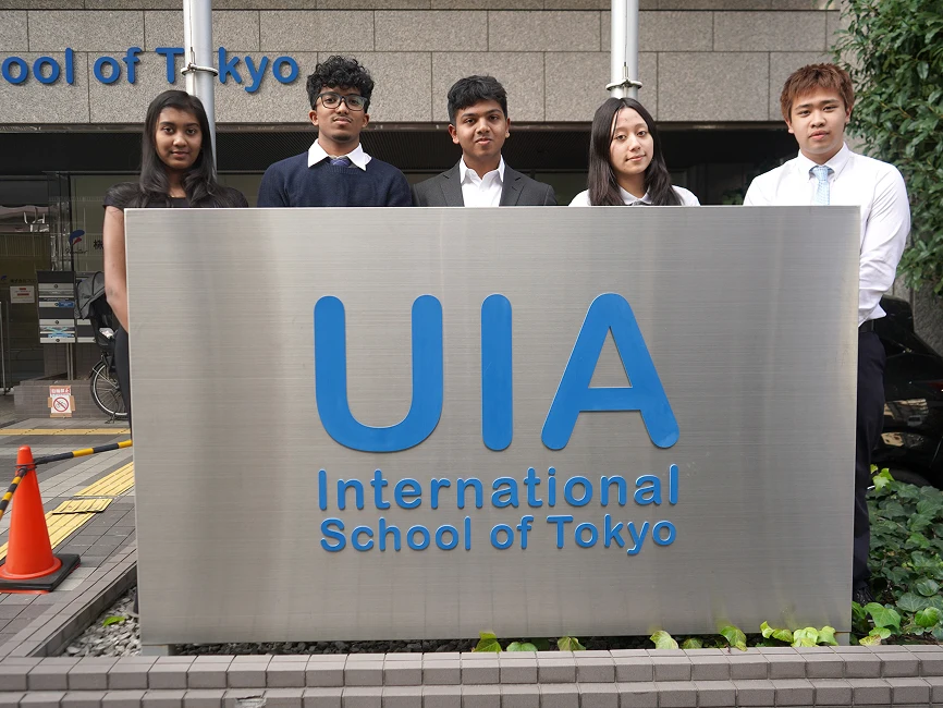 Students standing in front of UIA International School of Tokyo sign, showcasing diversity and unity.