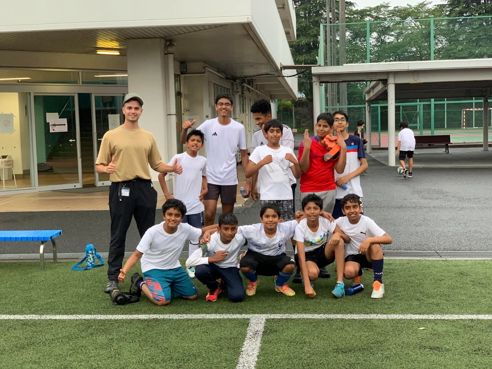 Group of young boys with an adult posing on a sports field, showing enthusiasm and teamwork.