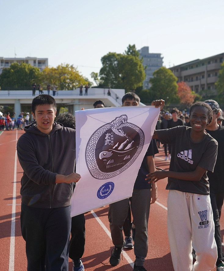Students holding a banner with a Genbu design during a school sports event on a sunny day.