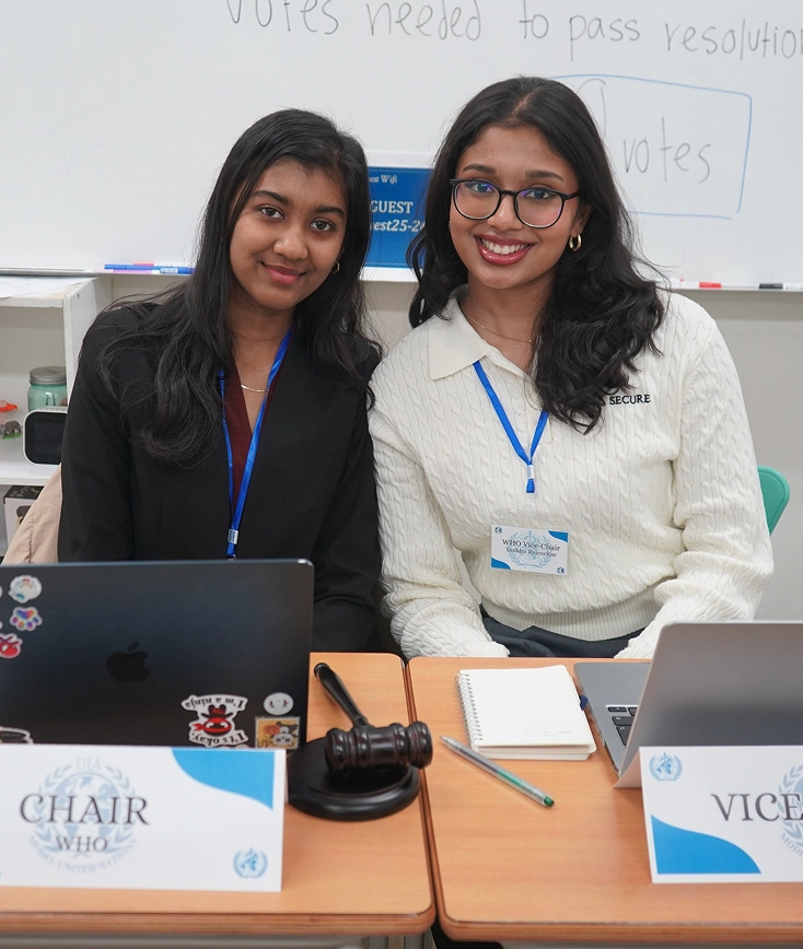Two delegates at a conference table, each with a laptop, wearing name tags and smiling, ready to chair a meeting.