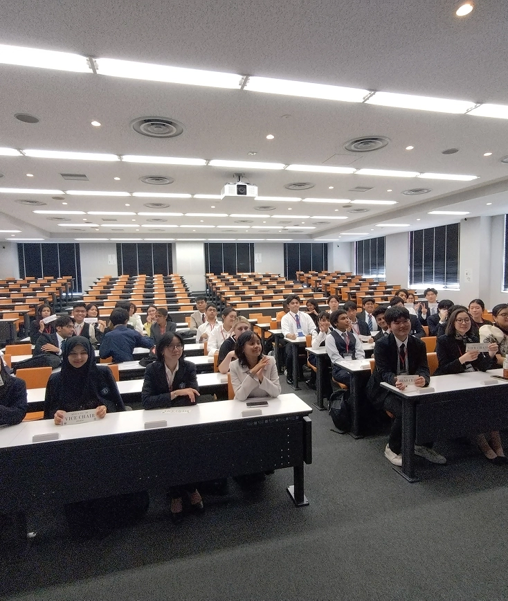 Students in a classroom setting, seated and facing forward, participating in an academic or conference event.