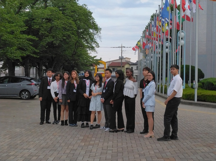 Group of young professionals standing on a paved area beside flagpoles, dressed in formal attire.