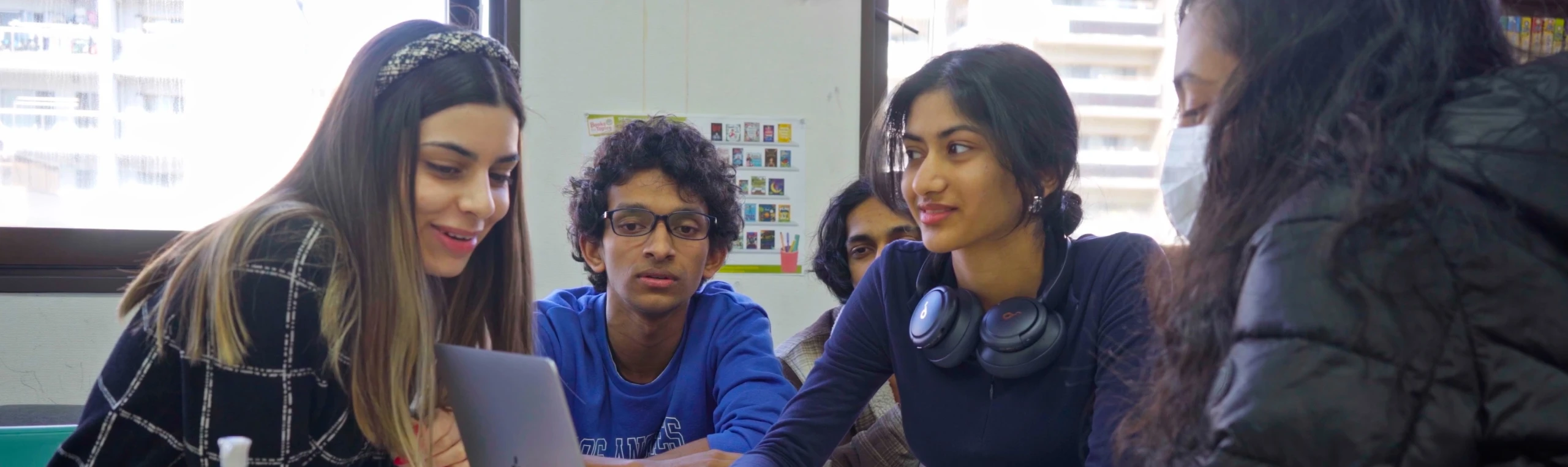 Group of students collaborating around a laptop in a classroom setting.
