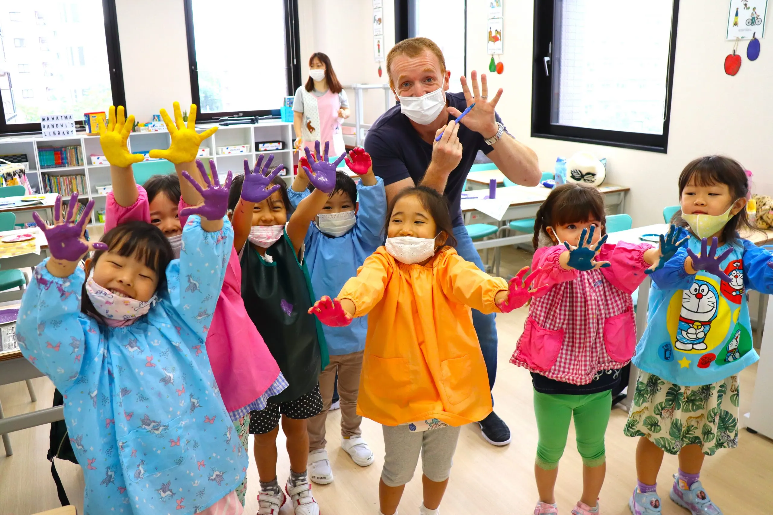 Children in colorful aprons showing painted hands in a classroom art activity, smiling and having fun.