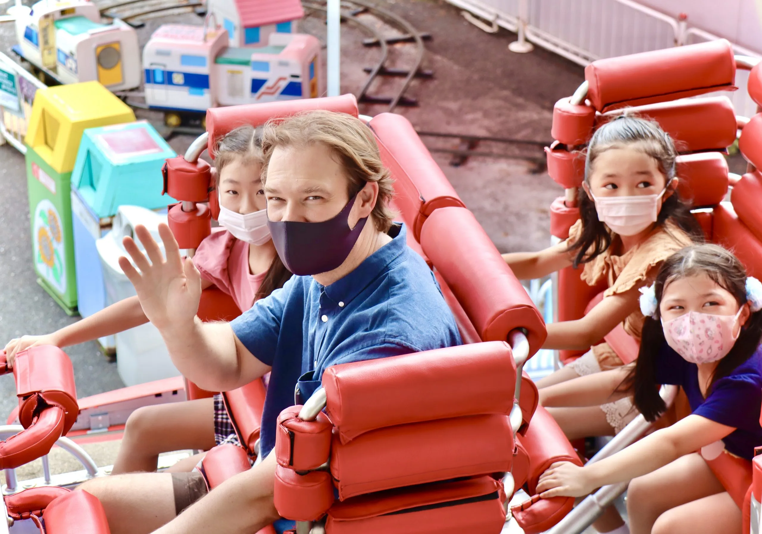 Masked group smiling on red amusement ride at fun park.