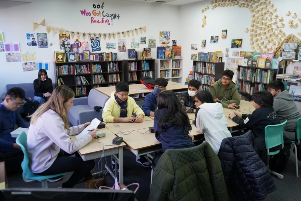 Students collaborating in a library, engaging in a group activity with books and notes around them.