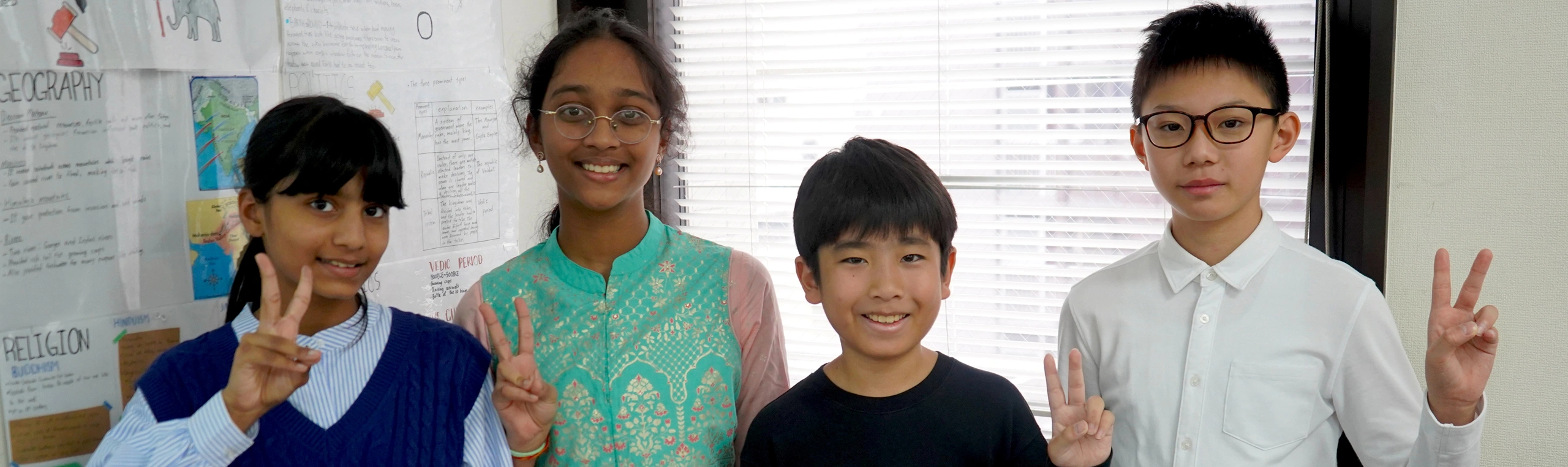 Group of smiling students posing with peace signs in front of educational posters.