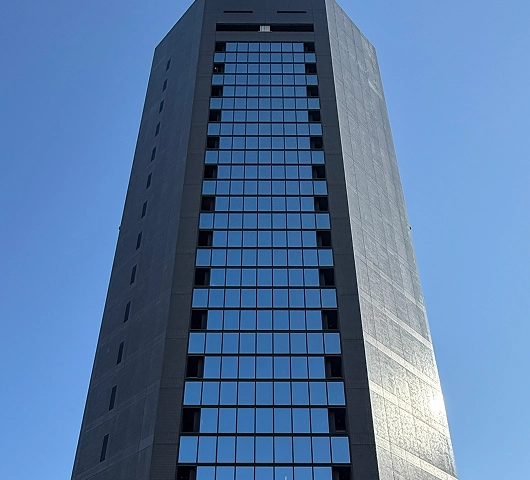 Modern skyscraper with glass windows against a clear blue sky, captured from a low angle perspective.