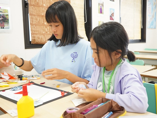 Children engaged in crafts at a classroom table, creating colorful art with paper, glue, and stationery.