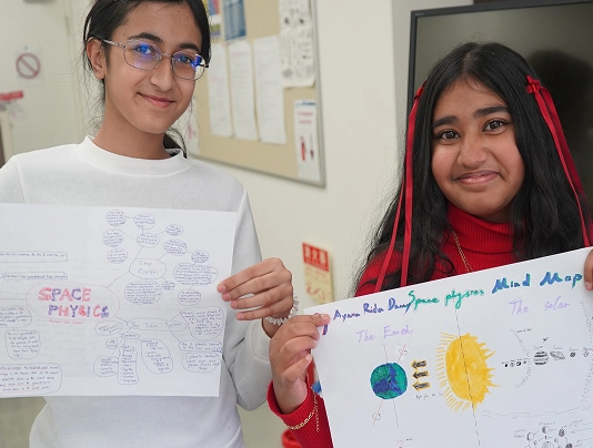 Two students proudly display their space-themed mind maps in a classroom setting.