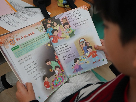 Child reading a colorful Hindi storybook in a classroom setting.
