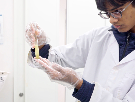 Scientist in a lab coat examines a test tube, wearing gloves for safety in a laboratory setting.